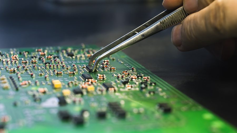 Close up photo of a person's hand placing a component onto a printed circuit board with curved tweezers.